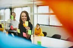 Two business women and a man in an office putting sticky notes on a window.