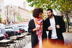 man and woman walking down the street with a coffee to go