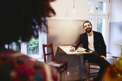 Man sitting at table with a coffee, smiling to someone