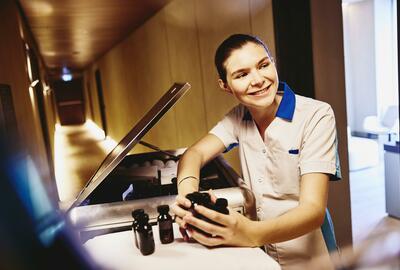 Woman in housekeeping uniform, holding small toiletries bottles.