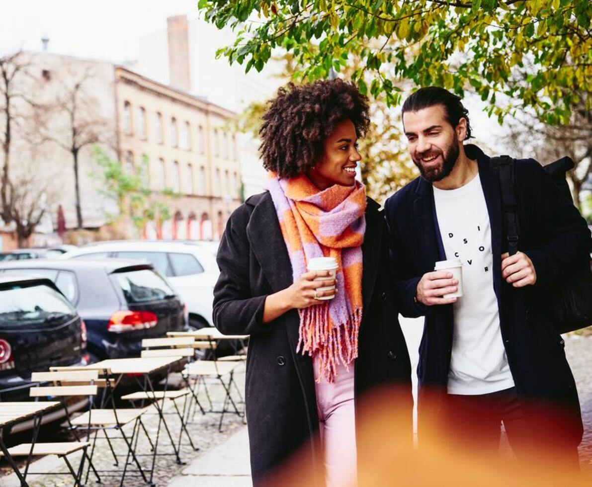 man and woman walking down the street with a coffee to go